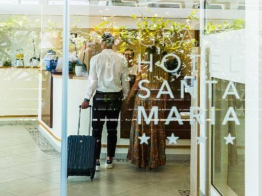 Entrance of the four-star Hotel Santa Maria, with elegant reception and guests arriving with luggage.
