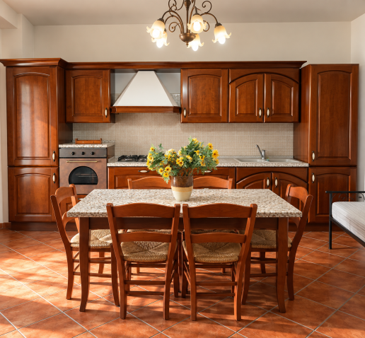 Cucina rustica in legno scuro con grande tavolo da pranzo, sedie in legno, piano piastrellato e fiori gialli al centro.