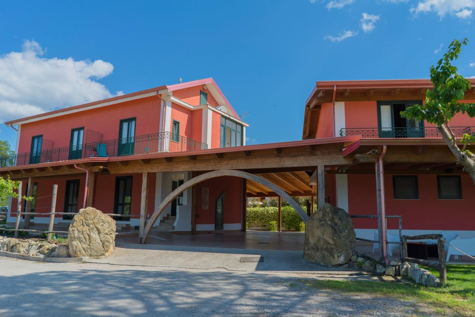 Extérieur de la ferme entouré de verdure, avec une grande terrasse.