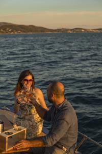 Coppia brinda con calici di vino su una barca al tramonto, immersa in un romantico paesaggio marino.