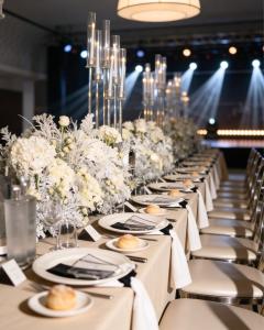 Allestimento elegante per evento con tavola imperiale, fiori bianchi, candelabri in vetro e sedute raffinate.