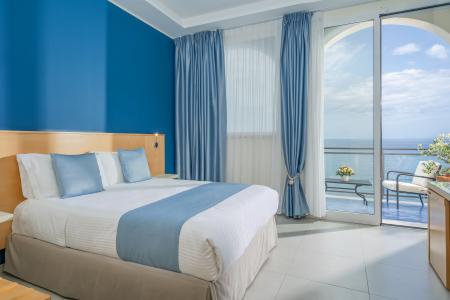 Hotel room with sea view with double bed, light blue furnishings and panoramic balcony overlooking the sea.