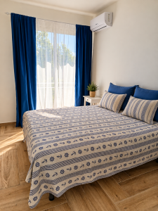 Chambre lumineuse avec lit double, rideaux bleus et blancs et draps de style nautique.