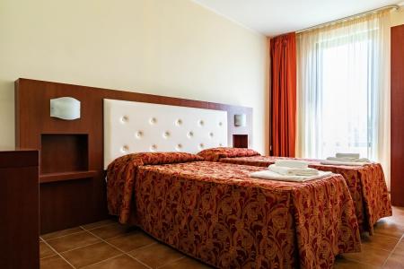 Camera da letto d’hotel con due letti singoli, biancheria decorata, testiera imbottita e tende arancioni.