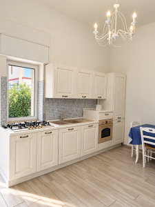 Cuisine lumineuse et moderne avec meubles blancs, plaque de cuisson, four, évier et table à manger.