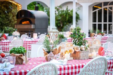 Tavoli apparecchiati con tovaglie a quadretti, decorazioni floreali e forno a legna in un elegante ristorante all’aperto.