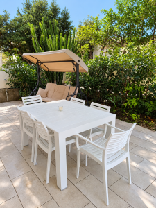 Mobilier de jardin blanc avec table et chaises, balançoire et plantes vertes sur une terrasse extérieure.