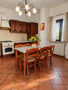 Cuisine rustique en bois sombre avec grande table à manger, chaises en bois, dessus carrelé et fleurs jaunes au centre.