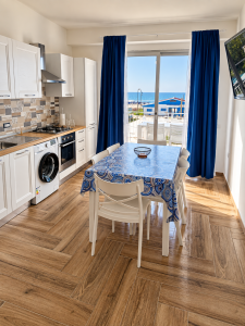 Cuisine moderne et lumineuse avec table à manger, rideaux bleus et vue sur la mer.