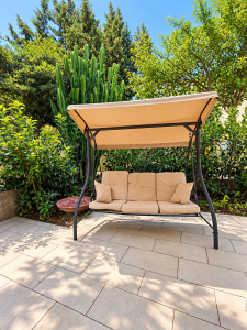 Balançoire de jardin avec structure en métal et coussins beiges, entourée de verdure.