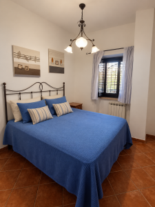 Chambre double de style rustique avec lit en fer forgé, linge de lit bleu, tables de chevet et fenêtre avec rideaux.